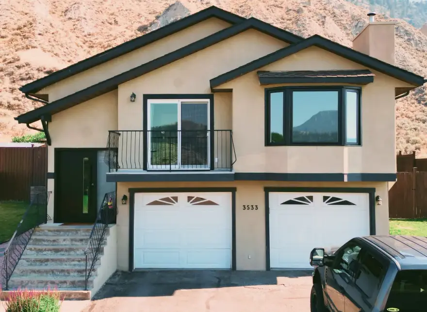 Tan stucco Alberta home with new black-framed windows and balcony door